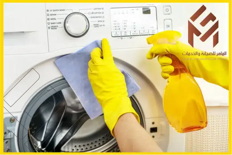رجل يقوم بتنظيف الغسالة بمادة تظيف مع قطعة قماش في الصورة فيها شعار الماهر للصيانة تنظيف الغسالة بانتظام