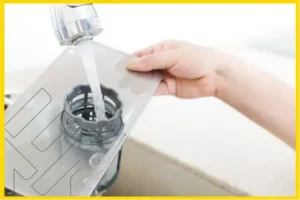 شخص يقوم بغسل فلتر غسالة الصحون تحت الماء من الصنبور، توجيهات ونصائح لصيانة غسالة الصحون وتصحيح الأخطاء الشائعة.