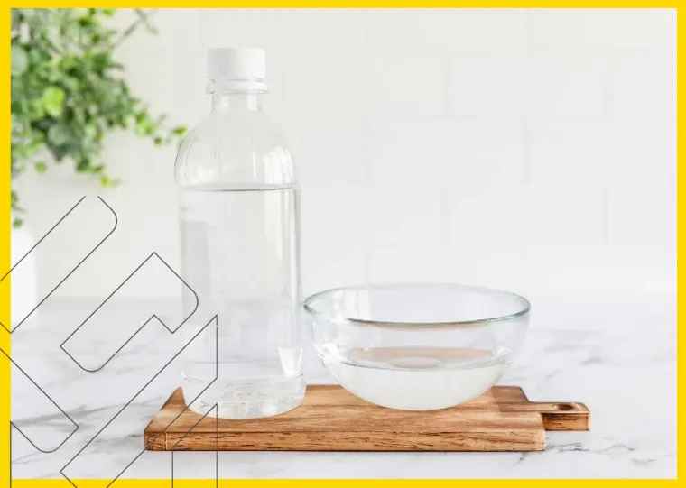 زجاجة ماء ووعاء زجاجي على لوح خشبي مع نبات في الخلفية. استخدام صابون الأطباق العادي