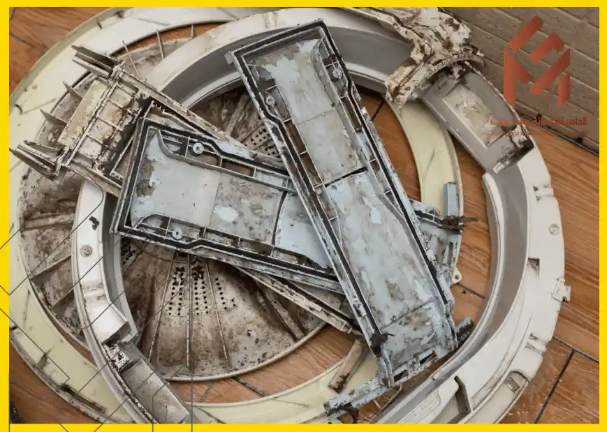 أجزاء معدنية قديمة ومتآكلة مكدسة فوق بعضها على أرضية خشبية.غسالة مفتوحة تُظهر لوحة التحكم الداخلية والأسلاك.كيف تخلي غسالتك تعيش معاك