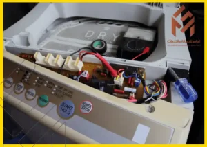 صورة تظهر الجزء الداخلي من غسالة LG معروض بشكل مفتوح للكشف عن اللوحة الإلكترونية والأسلاك الداخلية، ويظهر أيضاً مفك براغي. تُستخدم الصورة في سياق إصلاح عطل LE في الغسالة.