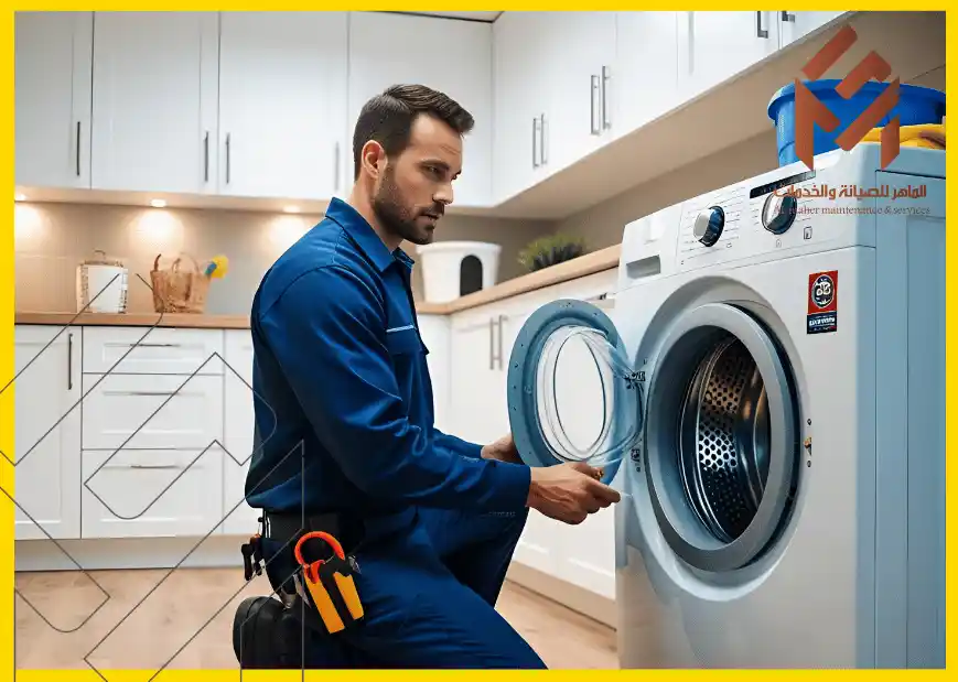 رجل يرتدي زي عمل أزرق يقوم بفحص غسالة في مطبخ عصري، مع عدة أدوات معلقة على حزامه.إصلاح الغسالة حلول لمشاكل الضوضاء وعدم تصريف الماء