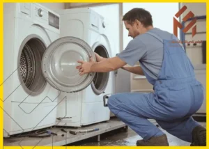 مهندس غسالات اتوماتيك بمكة يرتدي زي عمل أزرق يعمل على إصلاح غسالة ملابس بفتحة أمامية في غرفة غسيل.