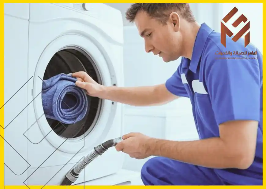 رجل يرتدي زي عمل أزرق يقوم بفحص أو تحميل منشفة زرقاء في غسالة ملابس بيضاء.مشكلات غسالات الملابس